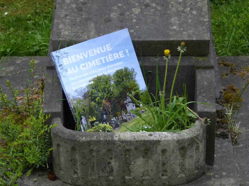 Le cahier pédagogique "Bienvenue au cimetière" est déposé dans une jardinière à l'avant d'un monument funéraire. 